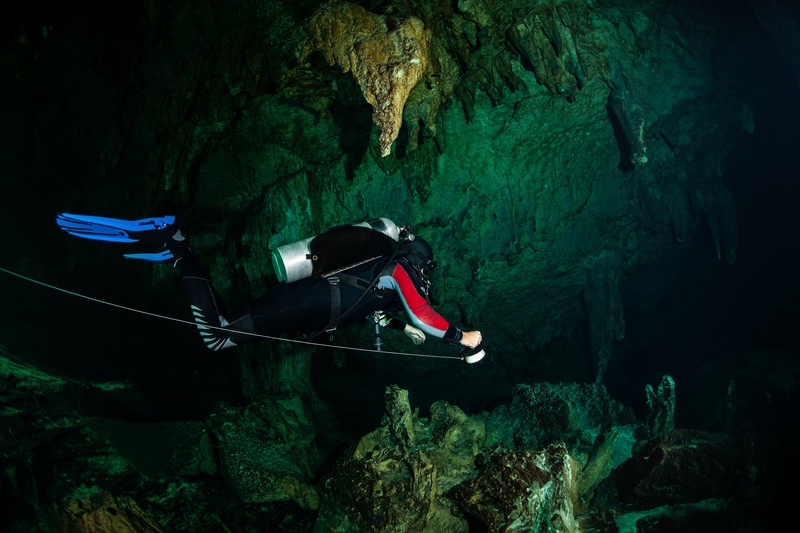 Red-suited cave diver follows the guideline through a cenote passage lined with stalactites.