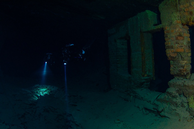 Cave diver illuminating old brick mine infrastructure with torch light in the flooded tunnels of Kleinenbremen mine.