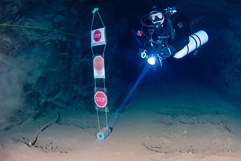 A diver illuminates a mine tunnel underwater, with stop signs marking a restricted zone in Kleinenbremen, Germany.